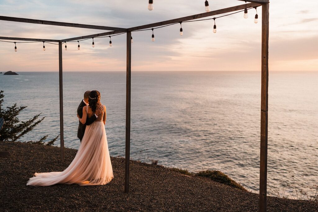Bride and groom hug while looking out over the ocean at their Airbnb wedding at Crook Point