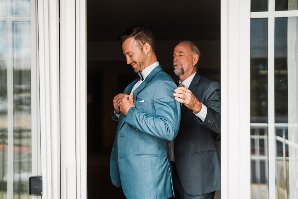 Father helping groom into his blue suit