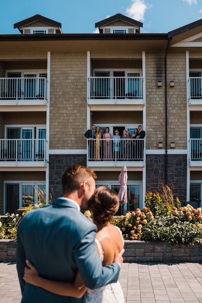 Bride and groom kiss after their wedding first look while loved ones look on from the hotel balcony