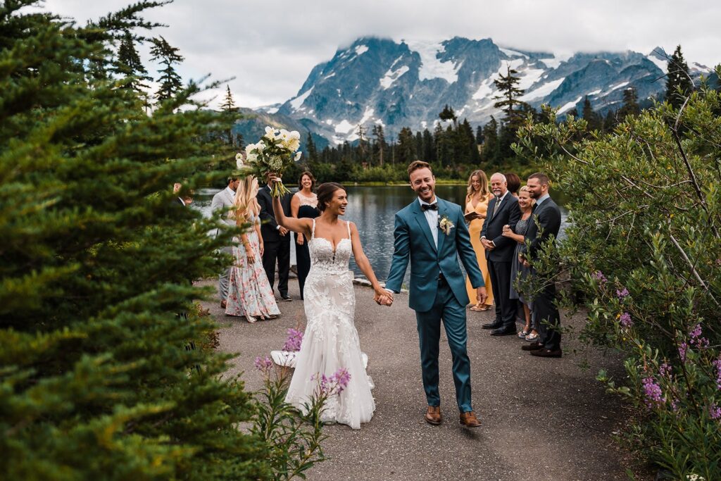 Bride and groom hold hands and cheer as they exit their outdoor wedding ceremony in the North Cascades