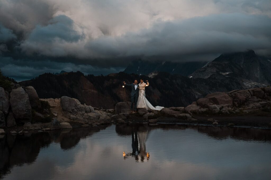 Bride and groom hold lanterns by the lake during their blue hour wedding photos 