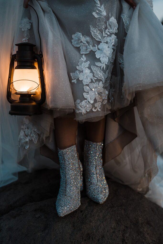 Bride holds lantern while holding up her wedding dress to show her sparkly wedding boots