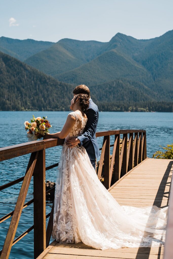 Bride and groom stand side by side on a wood bridge at their lake elopement in Olympic National Park