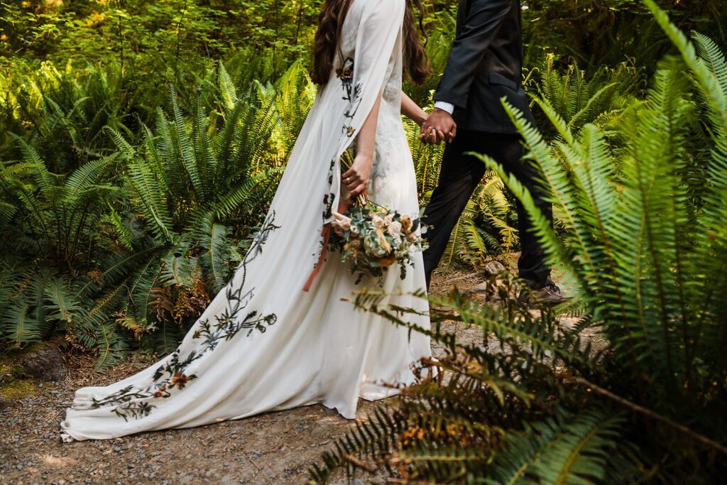 Bride and groom hold hands while walking through Hoh Rainforest during their Olympic National Park elopement