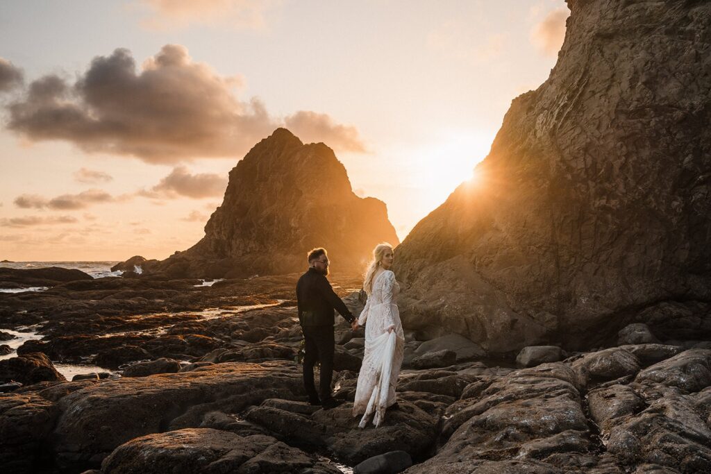 Bride and groom hold hands while walking across a rocky beach in Olympic National Park