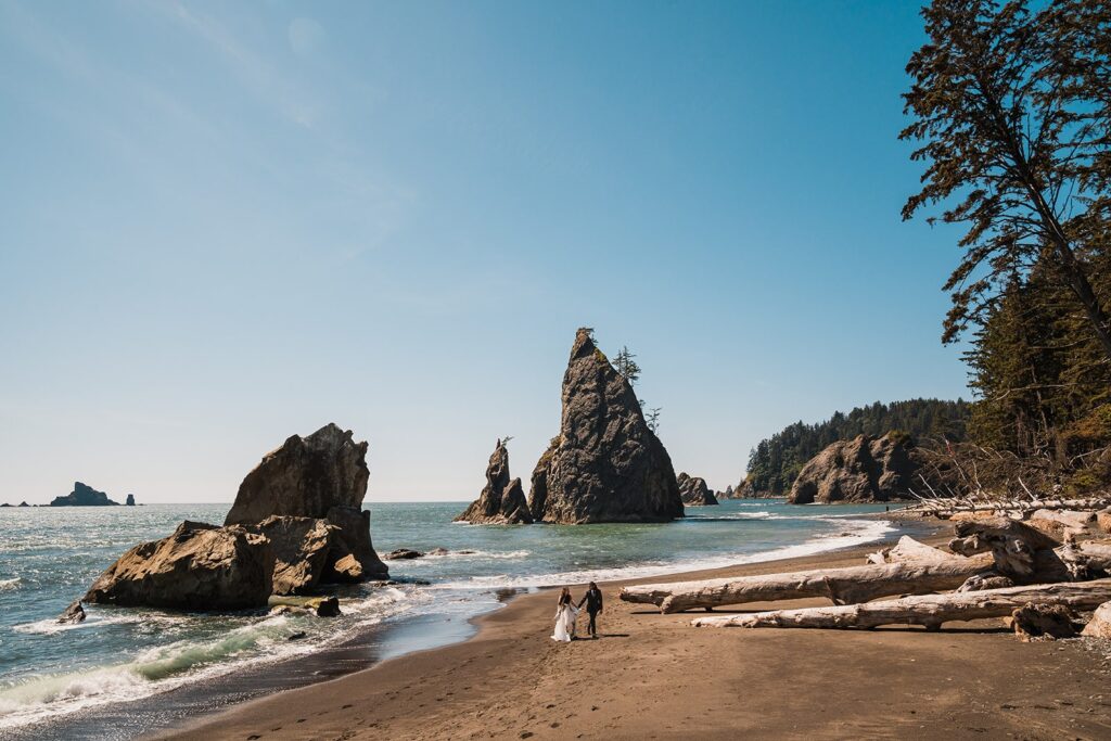 Bride and groom hold hands while walking across a beach at their Olympic National Park elopement