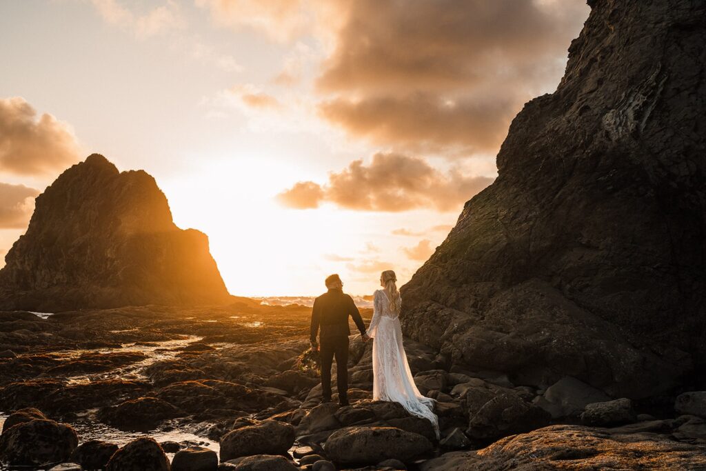 Bride and groom hold hands while walking across a rocky beach during their Olympic National Park wedding