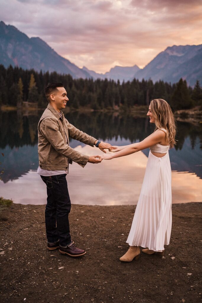 Bride and groom hold hands by a scenic lake during their sunrise adventure session in the PNW