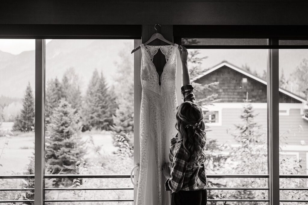 Bride reaching for her elopement dress hanging from a window at their Airbnb cabin