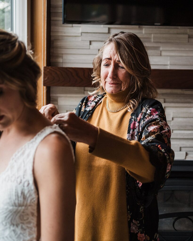 Mother of the bride getting emotional while helping her daughter into her wedding dress