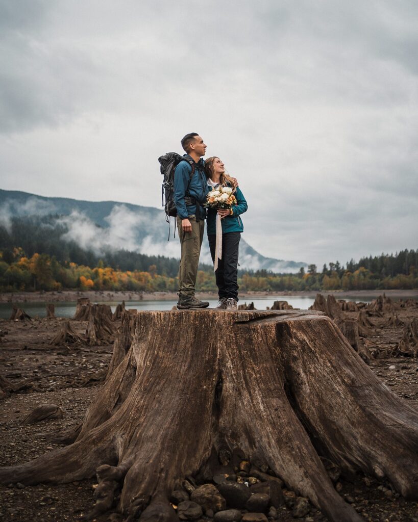 Bride and groom stand on a tree stump by a scenic lake during their Pacific Northwest elopement in Snoqualmie