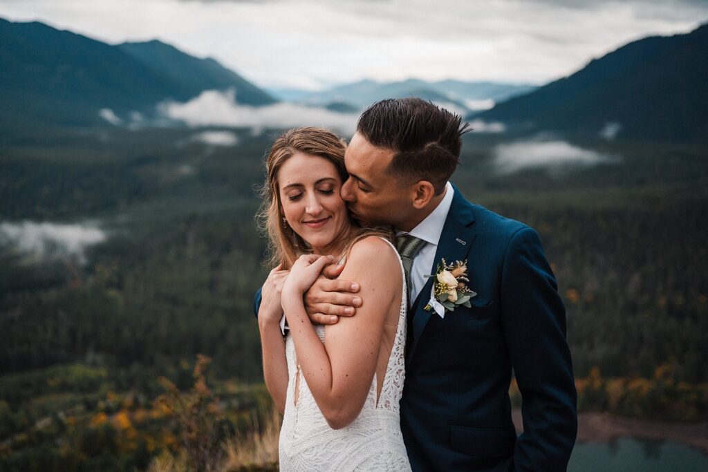Groom kisses bride during their Pacific Northwest elopement at a scenic overlook in Snoqualmie