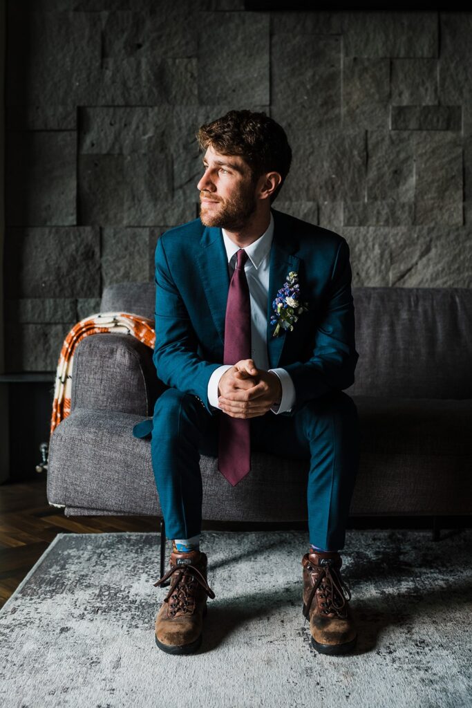 Groom wearing blue suit and burgundy tie sitting on a great couch at the Hotel Geysir in Iceland