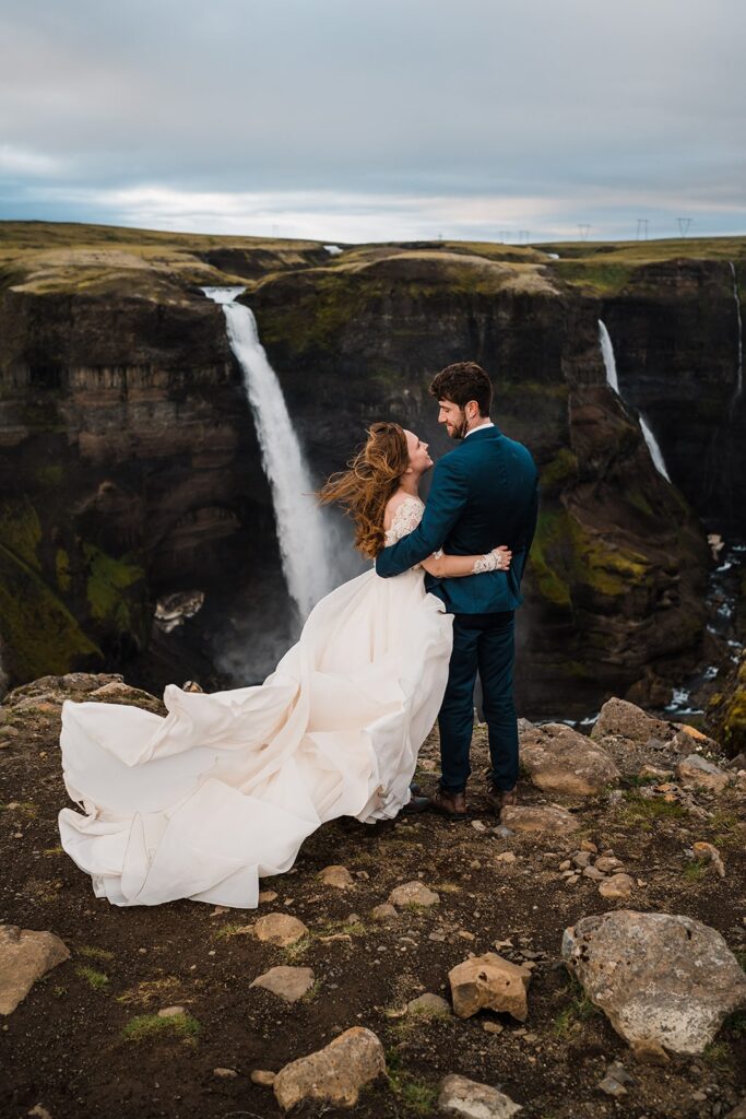 Bride and groom hug at the top of a waterfall overlook during their elopement in Iceland