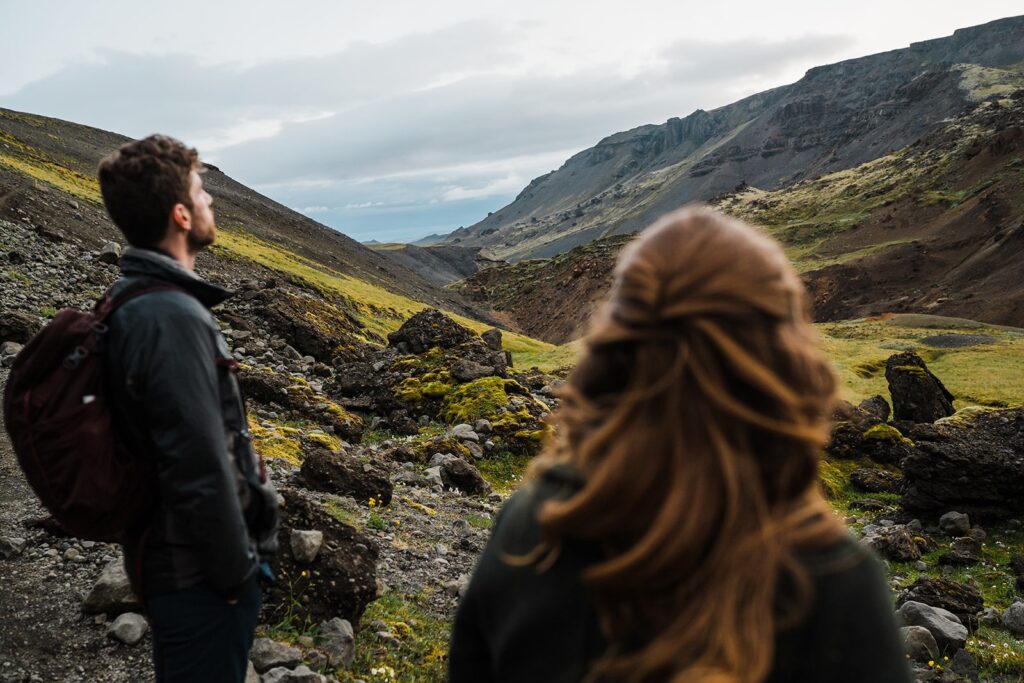Bride and groom look out over the mountains while hiking to a waterfall during their Iceland elopement