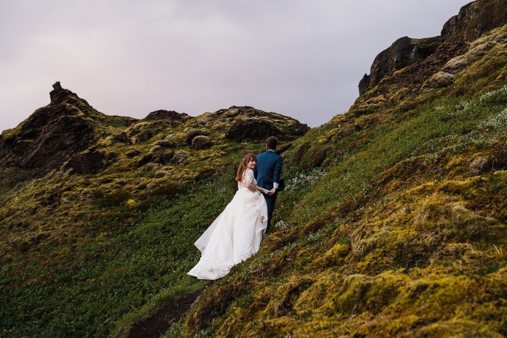 Bride and groom hold hands while hiking up a mountain trail during their Iceland elopement