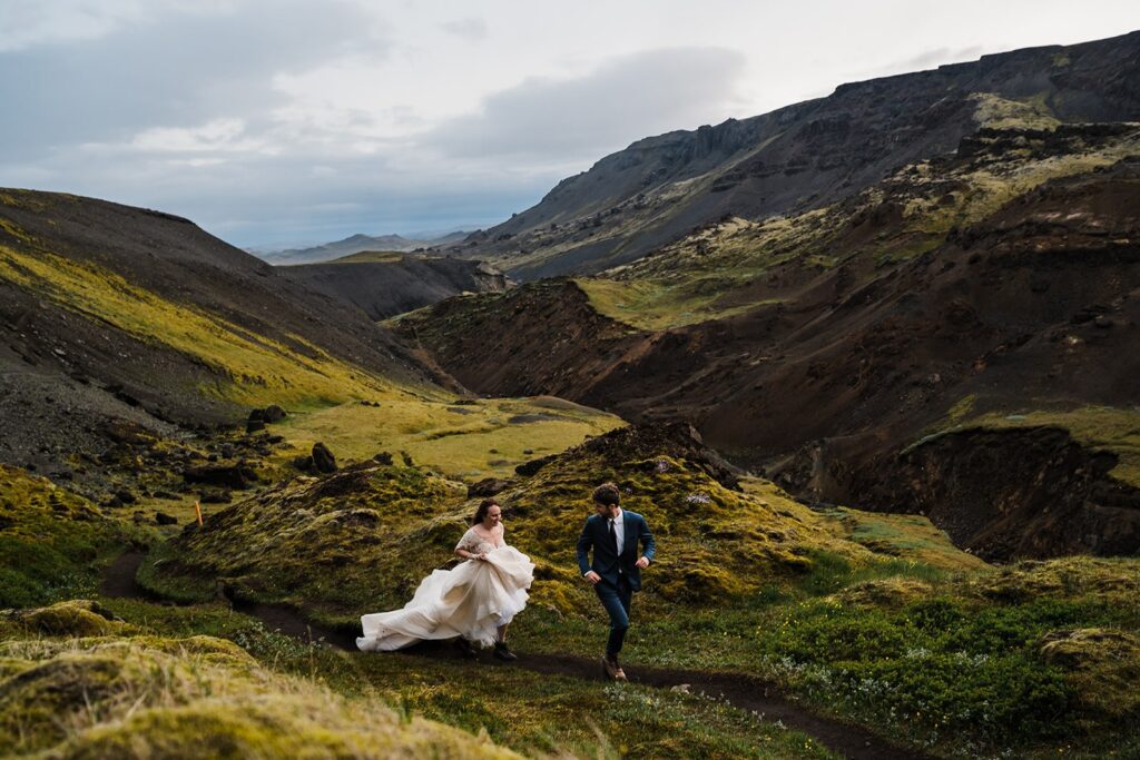 Bride and groom run along a hiking trail during their adventure elopement