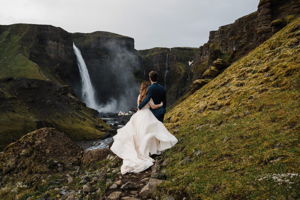 Bride and groom hug while looking out at a waterfall during their elopement in Iceland