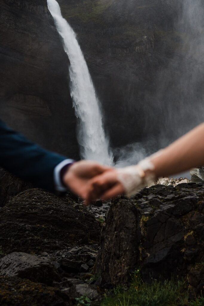 Bride and groom hold hands in front of a waterfall