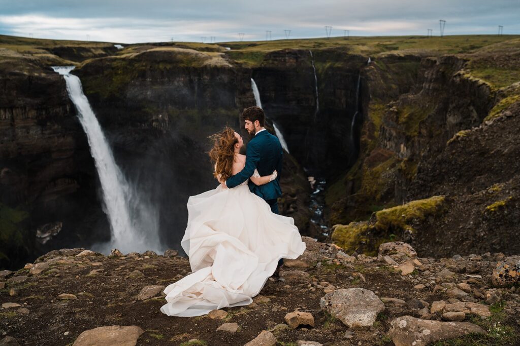 Bride and groom stand at the top of a waterfall overlook during their elopement portraits in Iceland