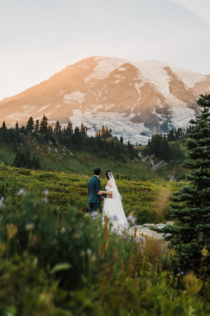 Bride and groom stand in a wildflower field looking out at Mt Rainier during their micro wedding in Washington