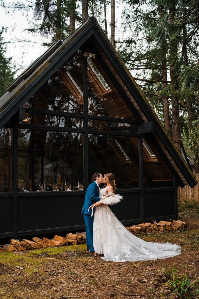 Brides kiss in front of an a-frame cabin at their wedding in Snoqualmie