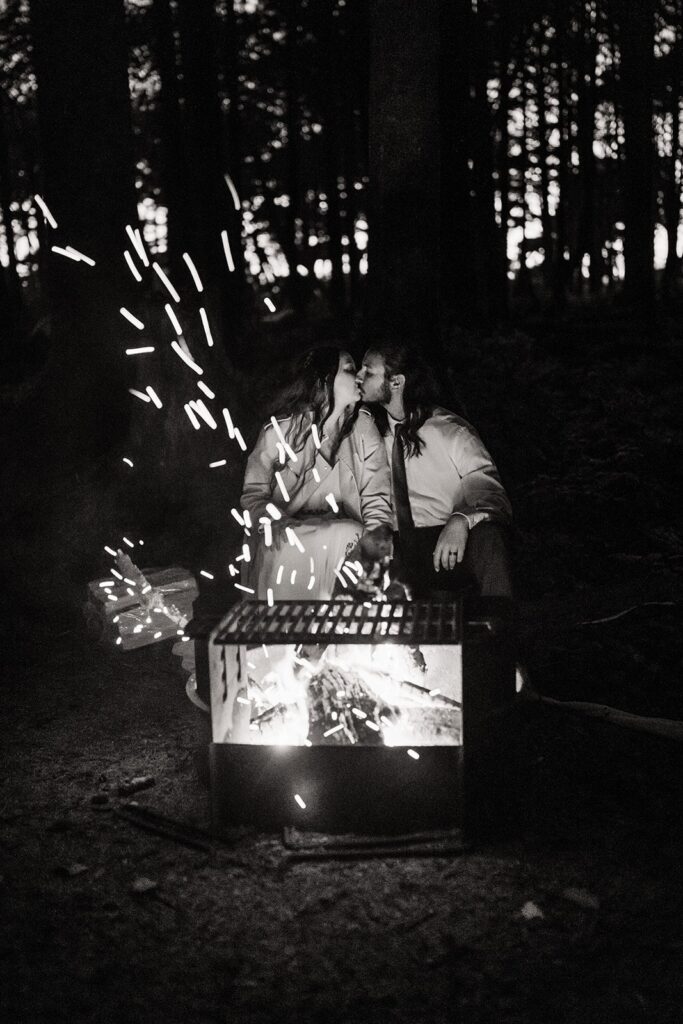 Bride and groom kiss in front of a camp fire at night