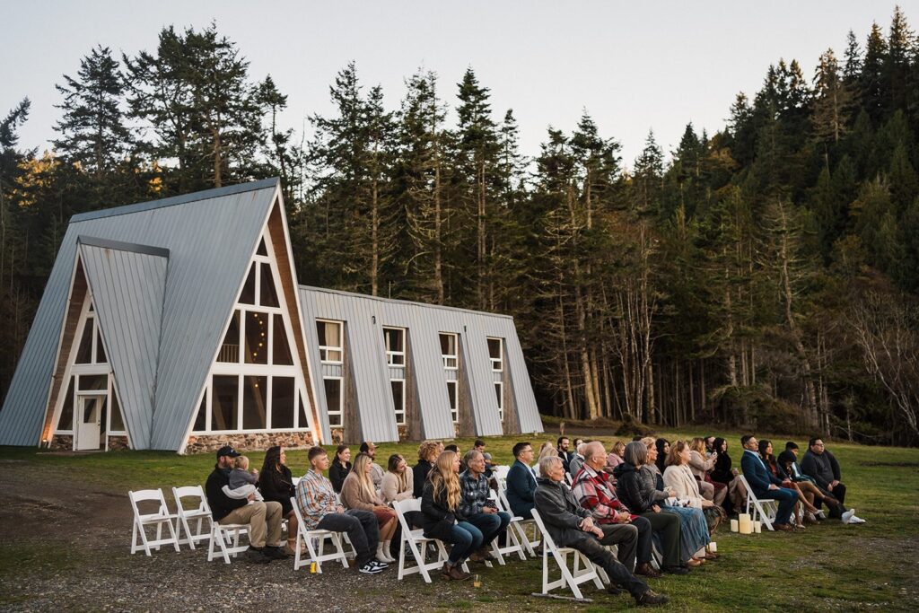 Guests sit in white chairs during an outdoor wedding ceremony by the beach on the Olympic Peninsula