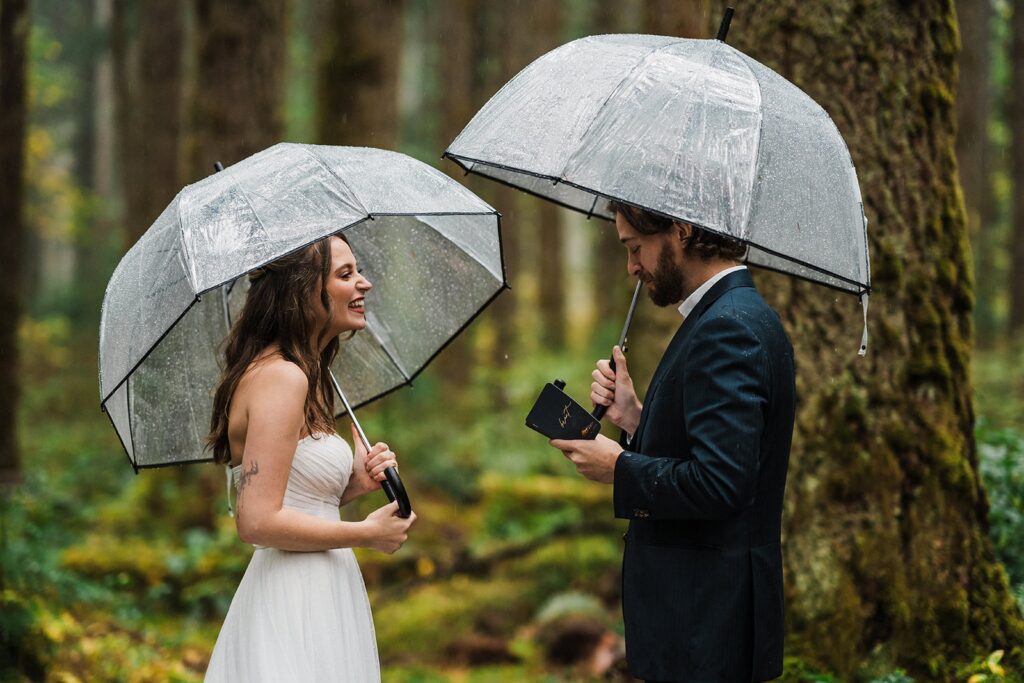Bride and groom exchange vows in the forest while holding clear umbrellas