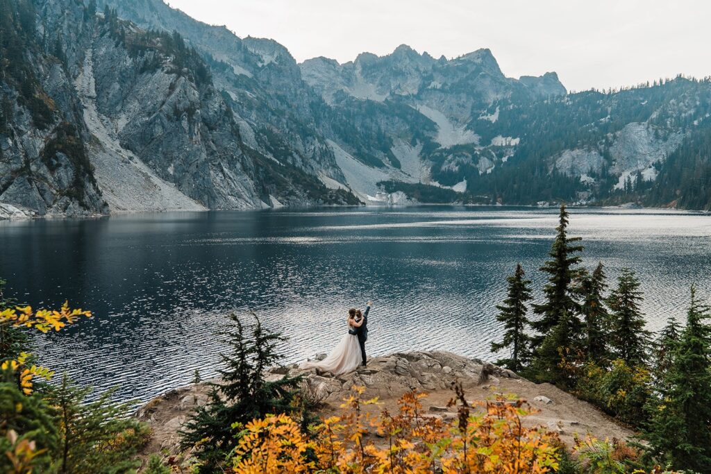 Bride and groom stand by a lake and point out at the mountains during their Snoqualmie elopement