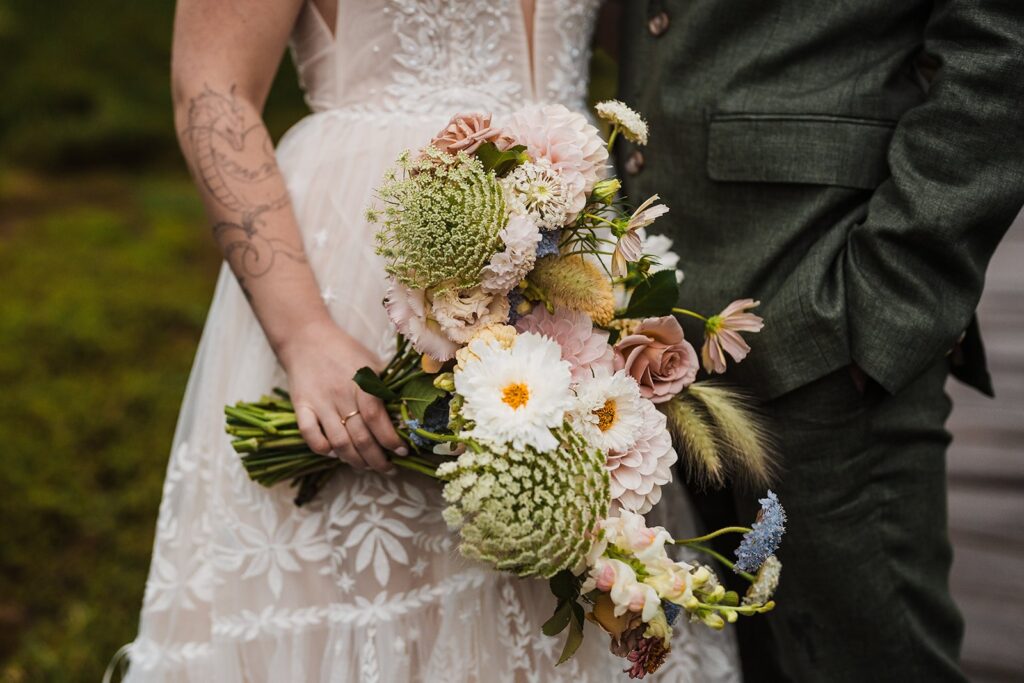 Bride holds a bouquet of green, white and light pink wedding flowers during her North Cascades wedding in the rain