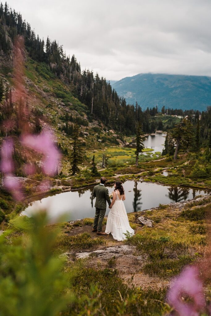 Bride and groom hold hands as they look out over an alpine lake in the North Cascades