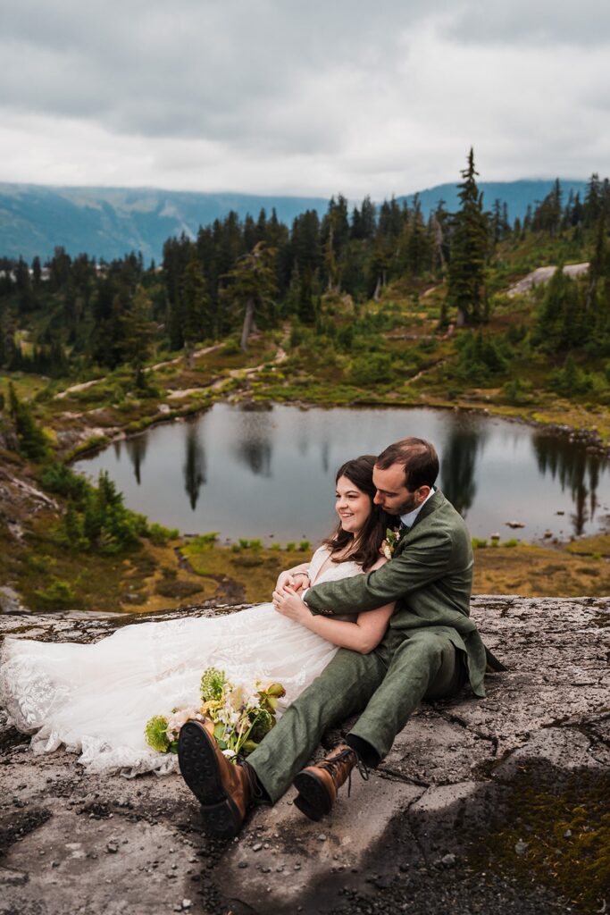 Bride and groom sit on a rock by an alpine lake at their North Cascades wedding