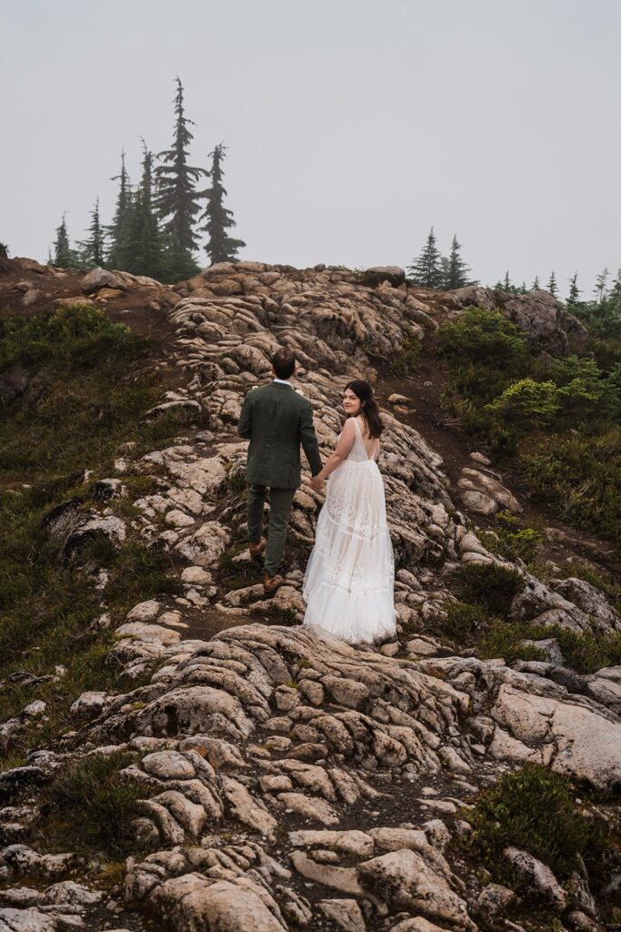 Bride and groom hold hands while hiking up a rocky mountain trail during their North Cascades wedding