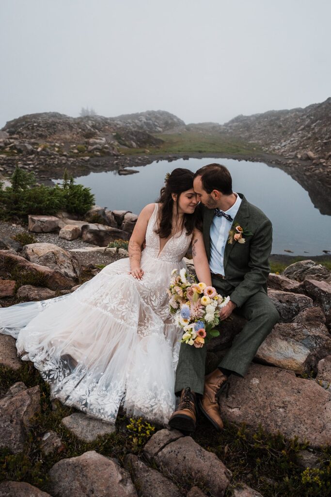 Bride and groom sit on a rock during their rainy wedding in the North Cascades