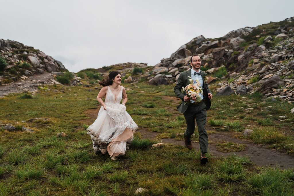 Bride and groom run through a field during their rainy wedding in the North Cascades