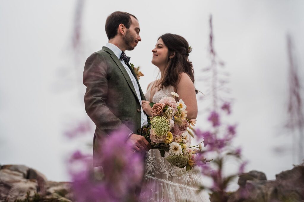 Bride and groom stand in a wildflower field during their rainy North Cascades wedding