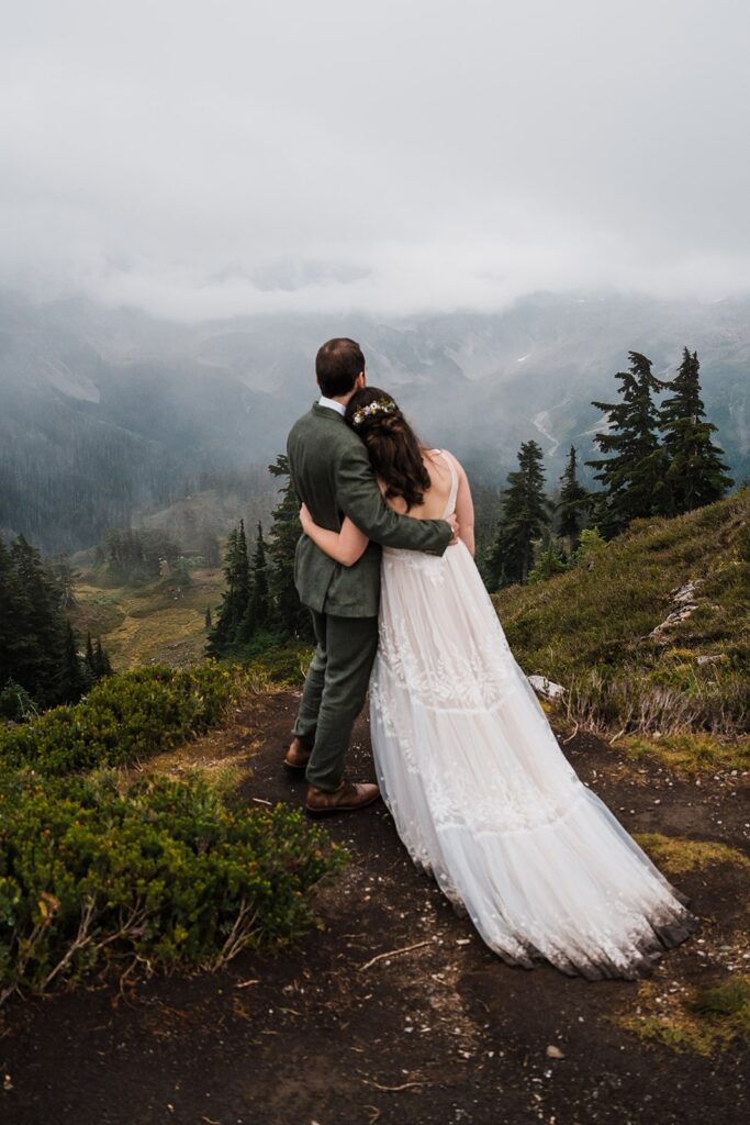 Bride and groom hug side by side looking out over the mountains at their rainy North Cascades wedding