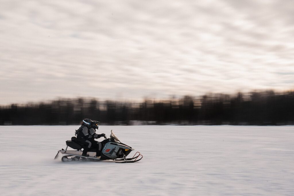 Couples speeds across the snow on a snowmobile during their elopement in Alaska