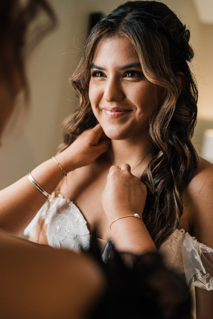 Bride smiles as mother helps her into her wedding attire 