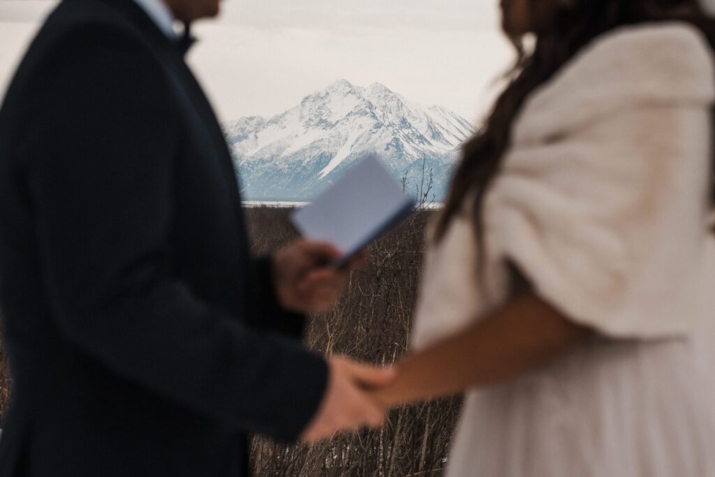 Bride and groom hold hands while reading private vows during their elopement in Alaska 