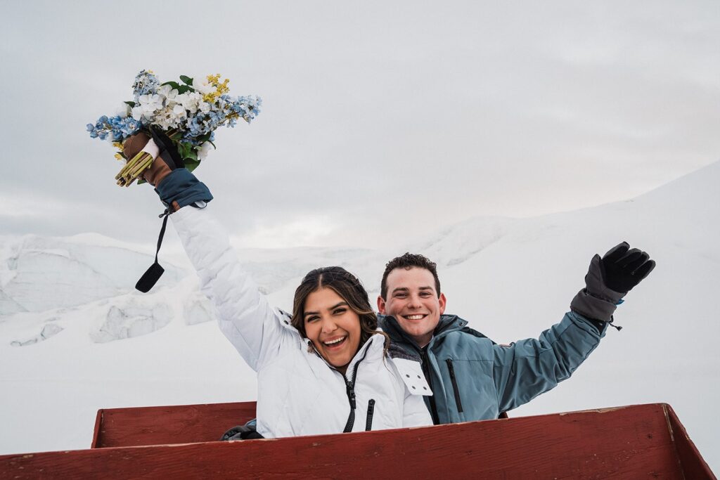 Bride and groom wave as they ride in a sled to their glacier elopement in Alaska