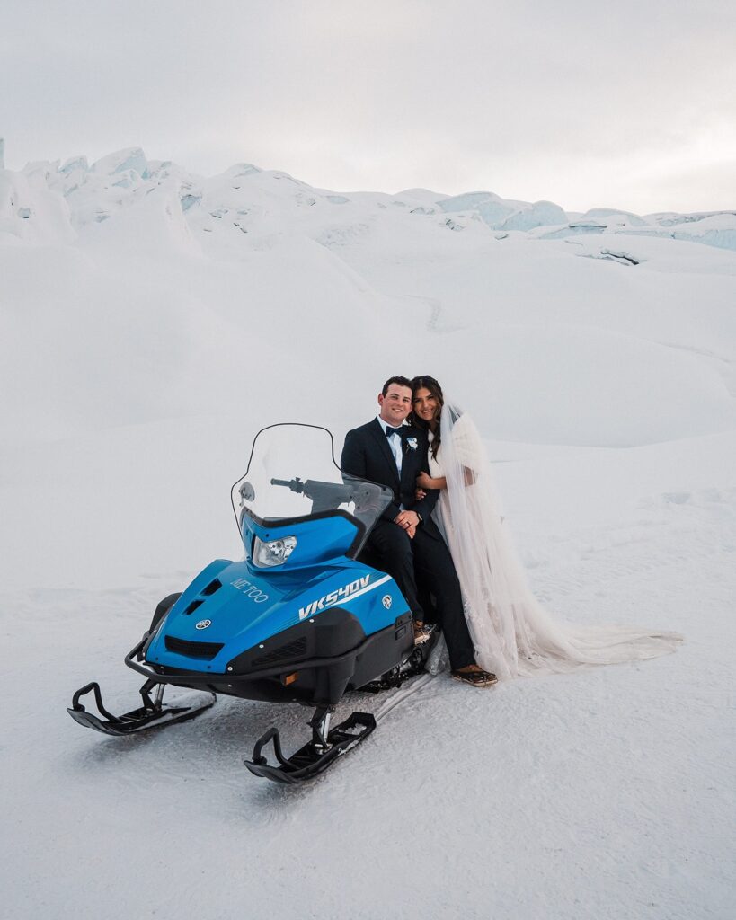 Bride and groom sit on a snowmobile during their glacier elopement in Alaska