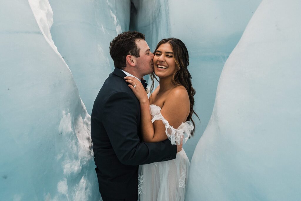 Groom kisses bride on the cheek in an ice cave during their Alaska glacier elopement