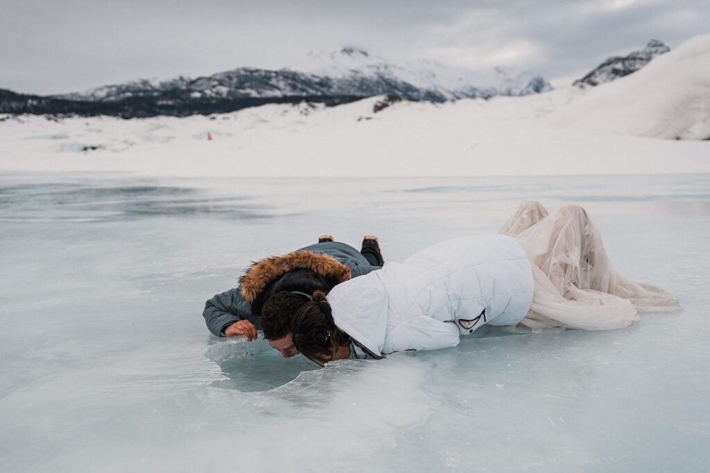 Bride and groom lay on the ground and drink water from a glacier 