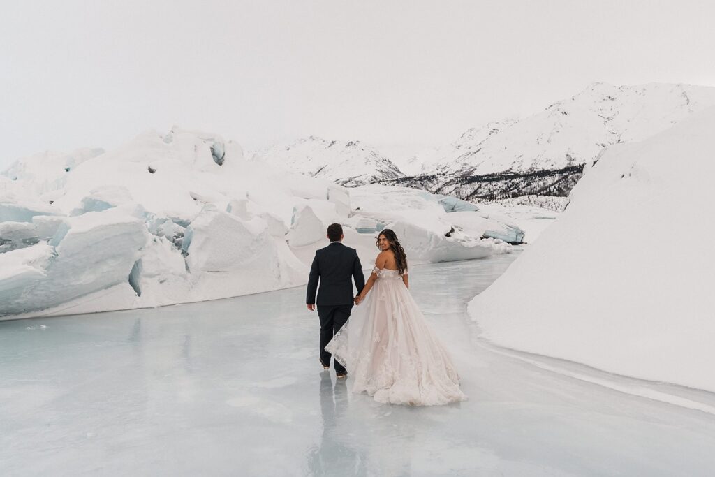 Bride and groom hold hands as they walk across an icy lake during their Alaska glacier elopement