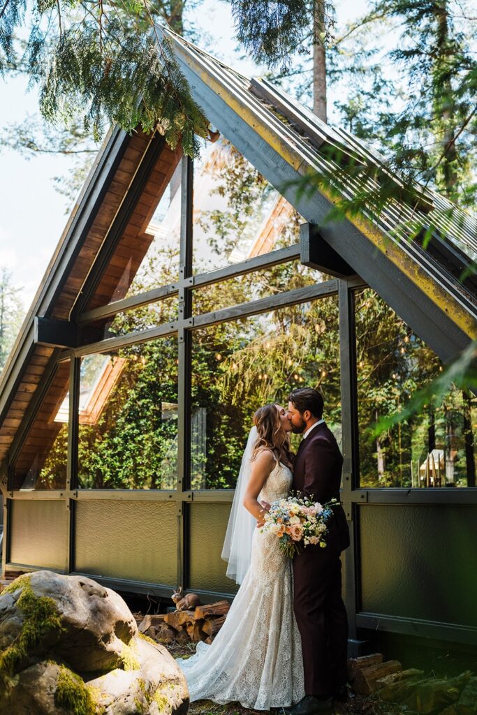 Bride and groom kiss in front of an A-frame cabin micro wedding venue in Washington