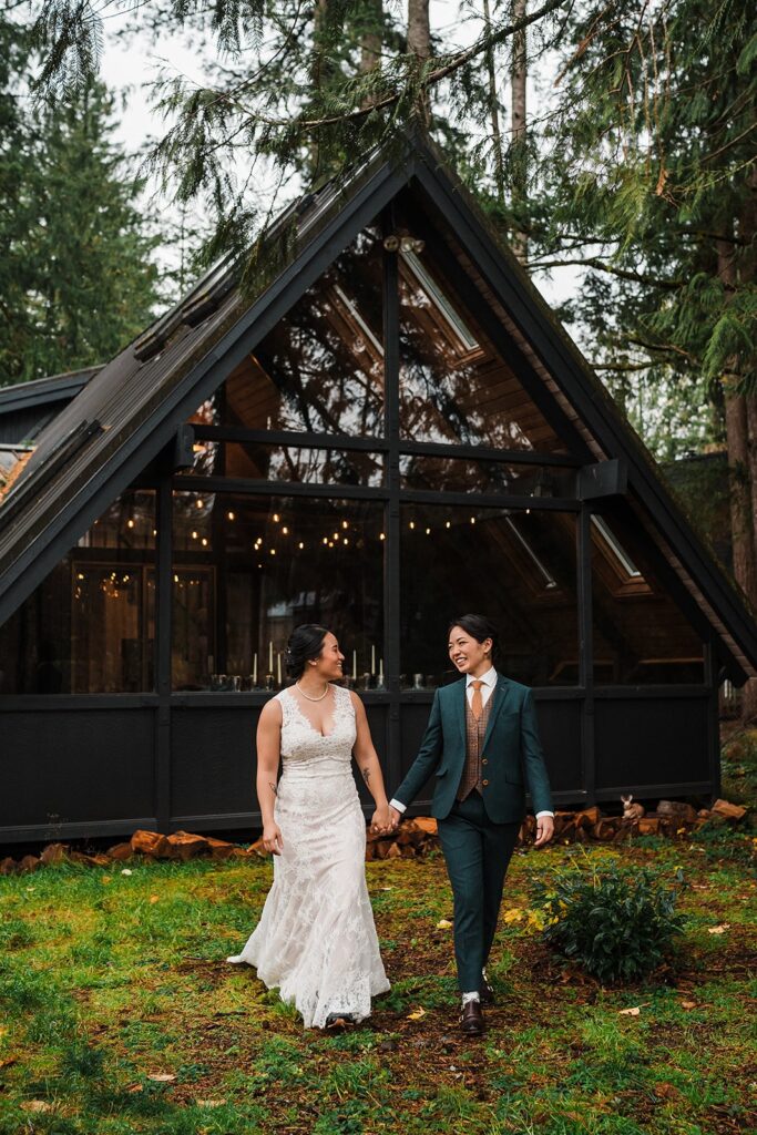 Brides walk hand in hand away from their A-frame cabin micro wedding venue in Washington