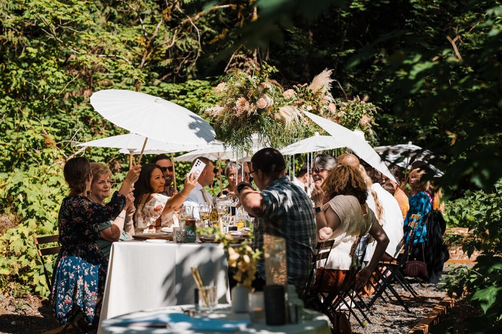 Guests hold parasol umbrellas at an outdoor wedding reception meal at Mt Baker Getaways