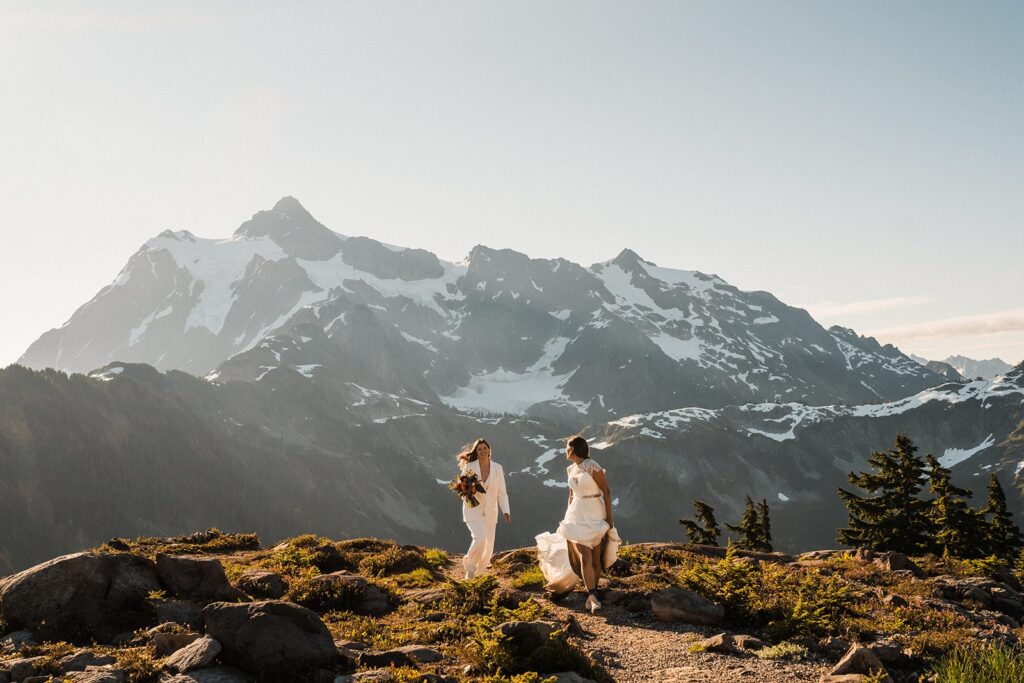 Brides run across a mountain trail during their North Cascades adventure elopement